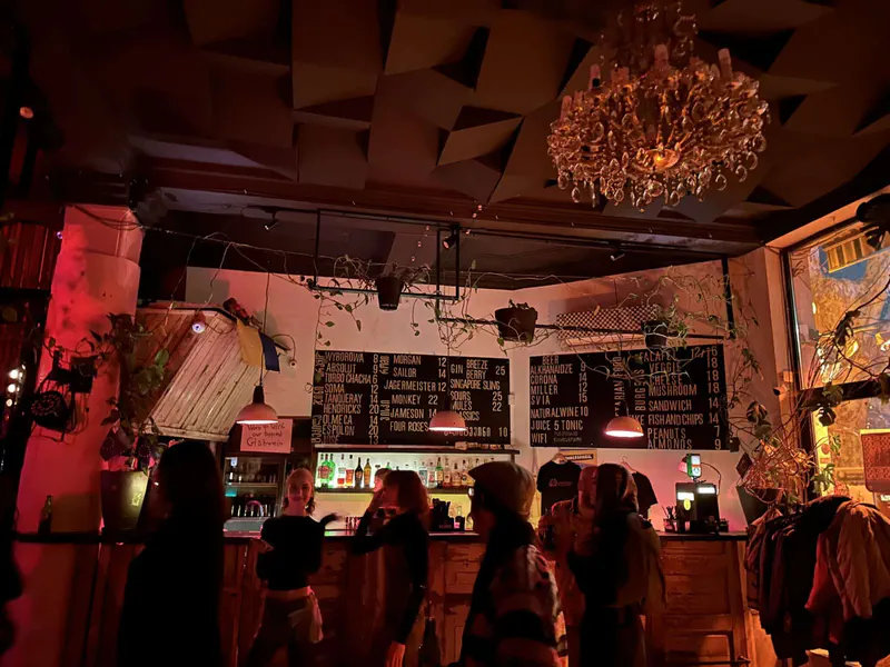 The warmly lit bar inside Dedaena, with a chandelier, plants and guests gathered beneath red light.