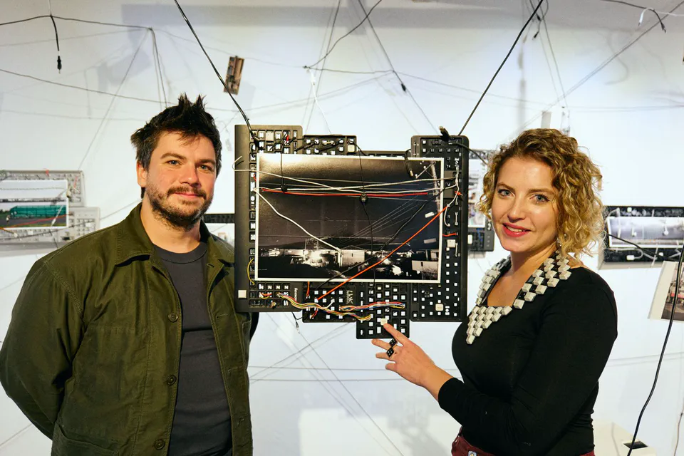Ludo and Toto standing beside a Wirescapes mixed-media artwork at UNTITLED SPACE in Tokyo, surrounded by photographs and suspended cables.