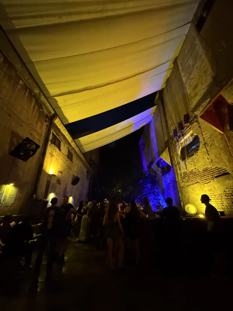 Guests talking beneath hanging fabric in yellow and violet courtyard lights at Mutant Radio.