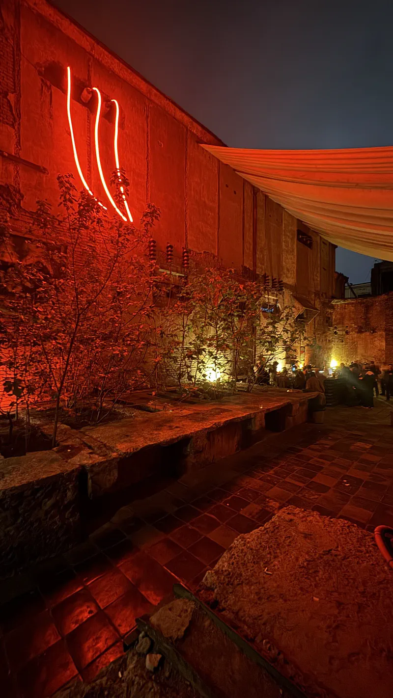 Mutant Radio's outdoor courtyard at dusk, with red neon, a fabric canopy, plants and tables.