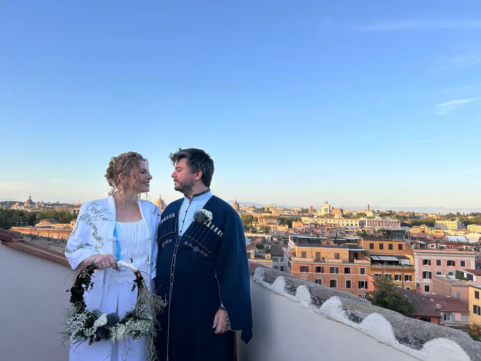 Ludo and Toto in their wedding clothes, smiling at each other on a rooftop overlooking Rome.