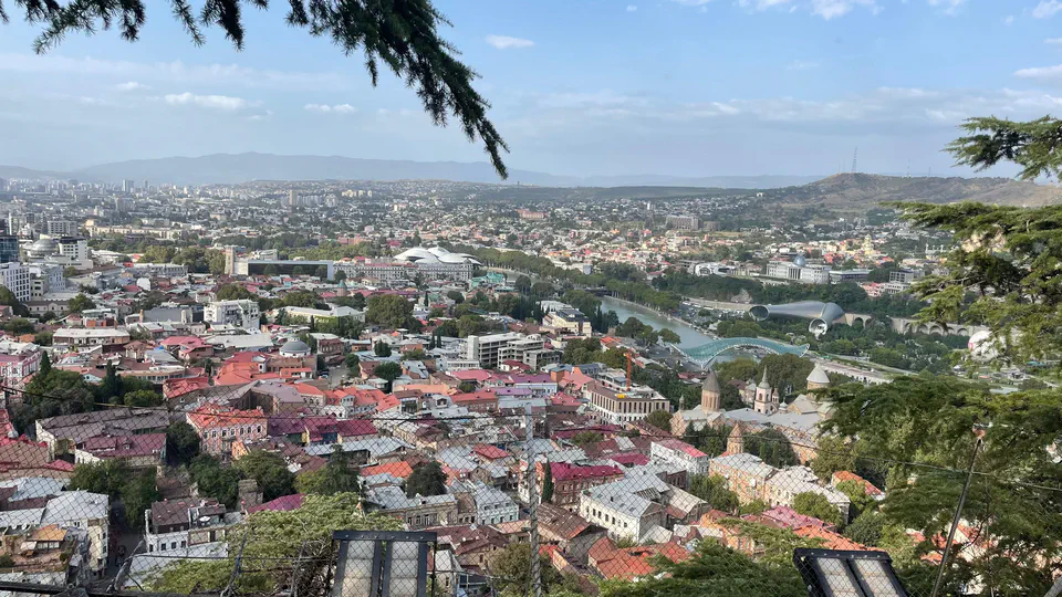 A wide daytime view across central Tbilisi, the Kura River and the city's hills.