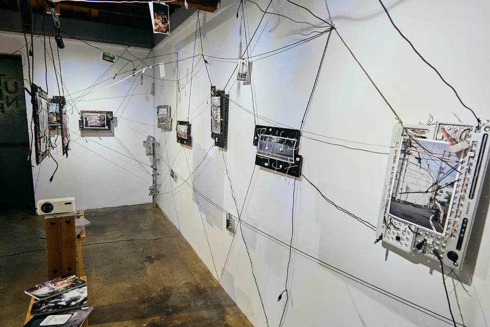 Wirescapes installation at UNTITLED SPACE in Tokyo: photographs and salvaged electronic components connected across white gallery walls by a web of black cables.